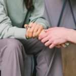 Close-up of two people holding hands during a comforting therapy session.